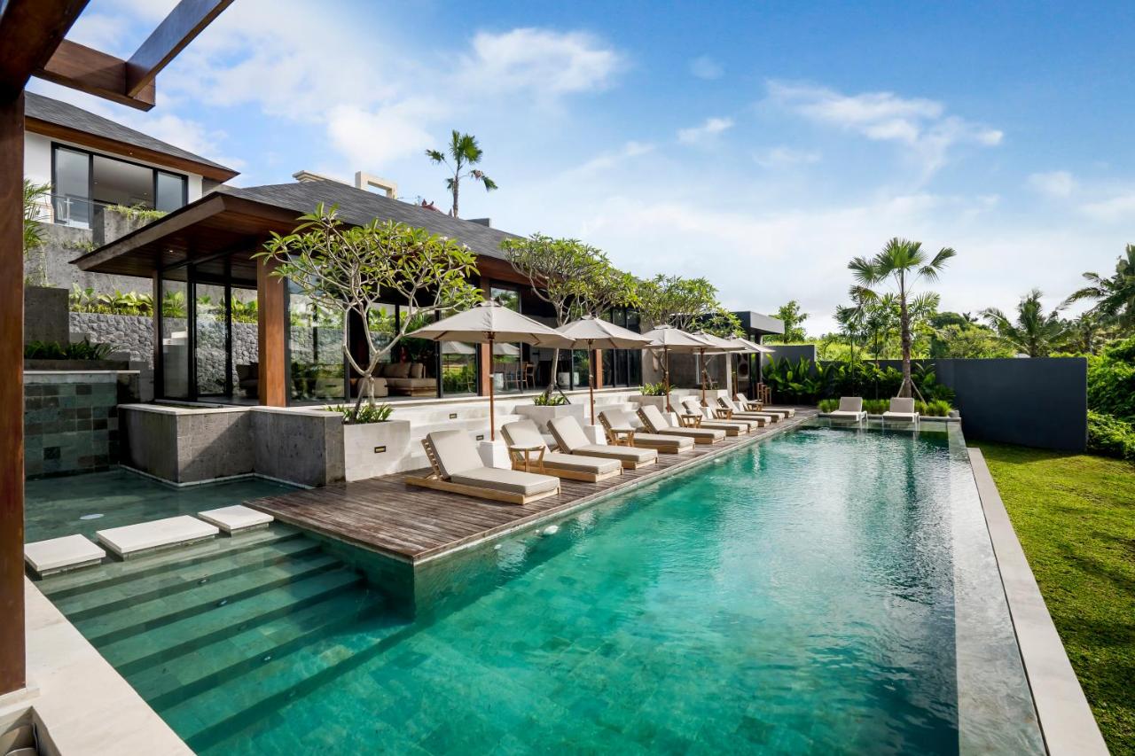 Modern villa with an infinity pool surrounded by sun loungers and umbrellas, elegant wooden decking, lush tropical foliage, under a clear blue sky